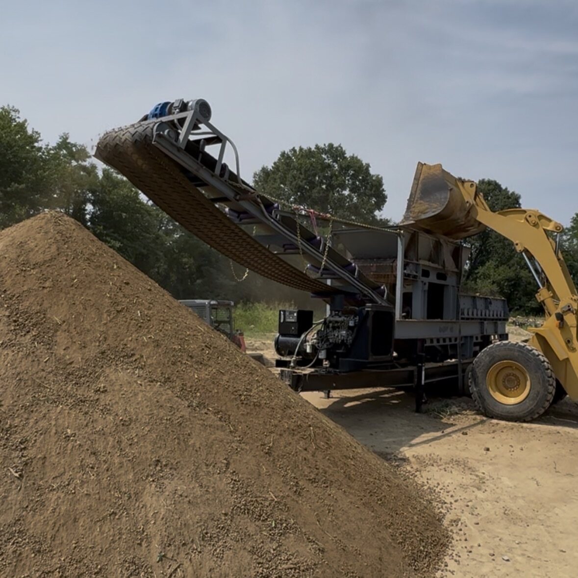 A loader feeding the screener at the Rocky Bottom Acres yard, with a pile of screened material.